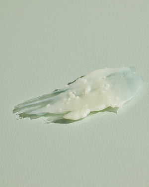 Close-up of creamy textured body salve with small granules on a light surface, representing Geranium Cedarwood BODY SALVE | Sparitual for skincare and body care.