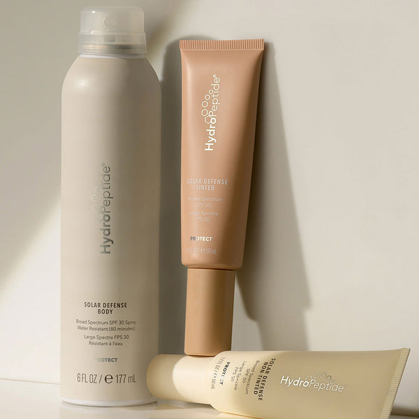 Three HydroPeptide skincare products arranged on a surface, featuring the Solar Defense Body SPF30 | HydroPeptide body spray among a moisturizer and another cream, highlighting body care and sun protection.