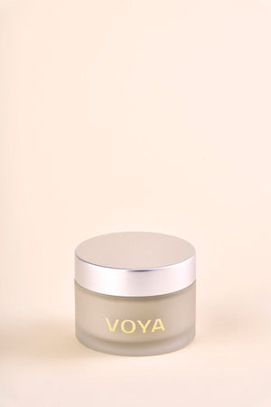 A frosted glass jar with a silver lid featuring the label VOYA, containing Get Glowing Illuminating Clay Mask | VOYA, a skincare product for radiant skin.