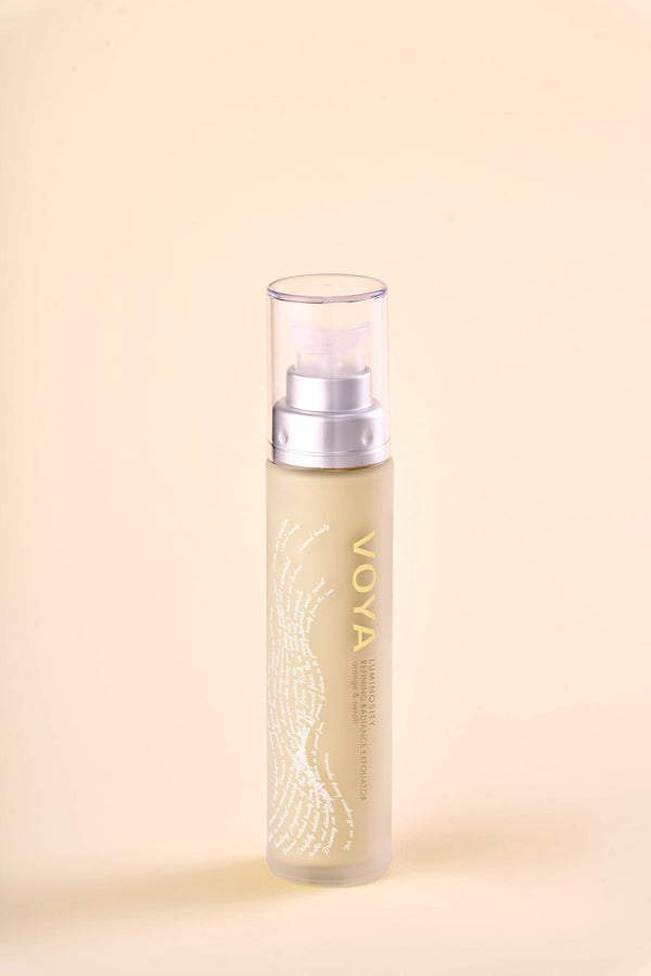 Clear pump bottle of Luminosity Refining Radiance Exfoliator | VOYA with gold lettering and subtle white design on a soft beige background, skincare product for radiance.