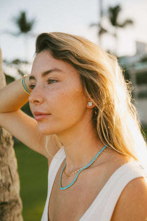 Close-up of a woman wearing gold dipped pearl studs | Meghan Bo Designs, with sunlit hair and a relaxed outdoor background.