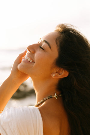Close-up of a smiling woman with eyes closed wearing Clear Quartz Earrings | Meghan Bo Designs, showcasing delicate clear quartz studs in natural sunlight.