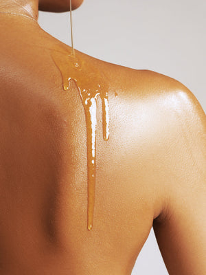 Close-up of golden body oil being poured onto the shoulder of a person with smooth skin, showcasing Pure Radiance Body Oil | True Botanicals for skincare and body care.