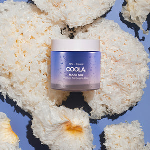 Moon Silk Moisture Recharging Mask | COOLA in a purple jar placed on white textured natural sponges, highlighting skincare and organic body care elements.