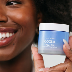 Close-up of a smiling person holding a jar of Moon Silk Moisture Recharging Mask | COOLA skincare product, highlighting hydration and wellness care.