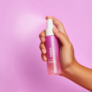Hand holding a pink spray bottle of Rewakening™ Rosewater Mist Face Spray | COOLA against a soft pink background, highlighting skincare and wellness.