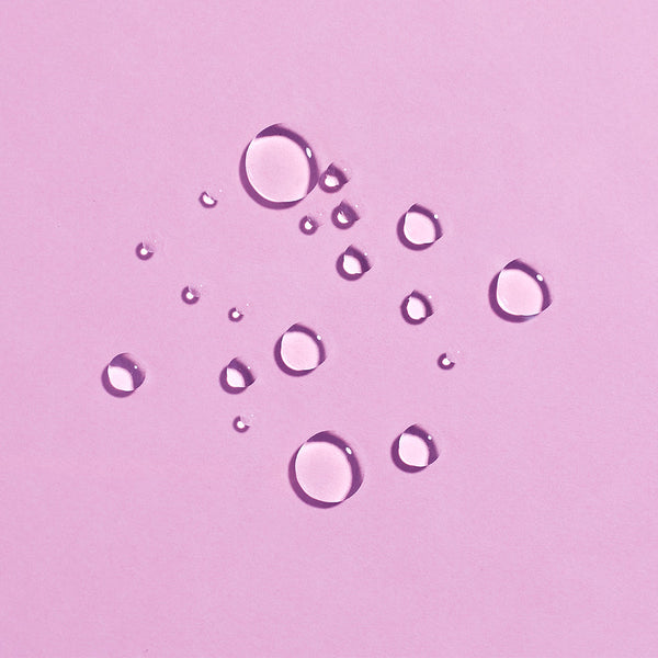 Close-up of clear water droplets on a soft pink surface representing hydration and freshness for Rewakening™ Rosewater Mist Face Spray | COOLA skincare.