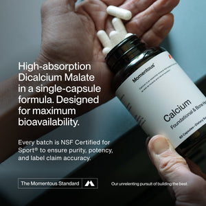 Hand holding white capsules pouring from a Momentous branded bottle labeled Calcium, highlighting high-absorption Dicalcium Malate in a single-capsule formula for maximum bioavailability and sport-certified purity.