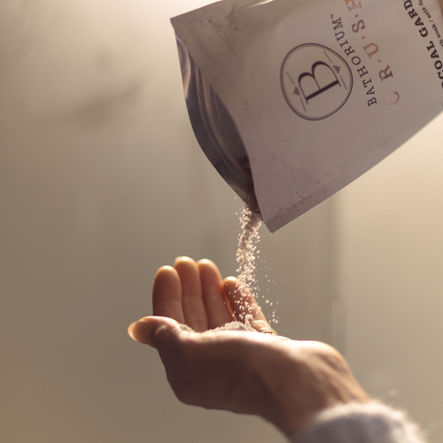 Hands catching fine granules being poured from a pouch labeled Charcoal Garden Detox Crush | Bathorium, highlighting body care and wellness supplements for skincare rituals.