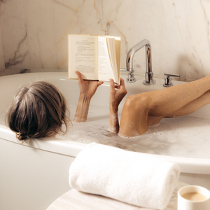 Person relaxing in a marble bath filled with bubbles, reading a book, showcasing a peaceful moment that complements the Charcoal Garden Detox Crush | Bathorium experience for wellness and body care.