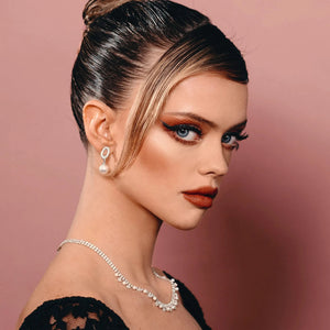 Close-up of a woman with dramatic eye makeup and long lashes wearing pearl earrings and a sparkling necklace, showcasing bold lashes likely enhanced by Drama & Shade Mini Mascara Set | Chella.