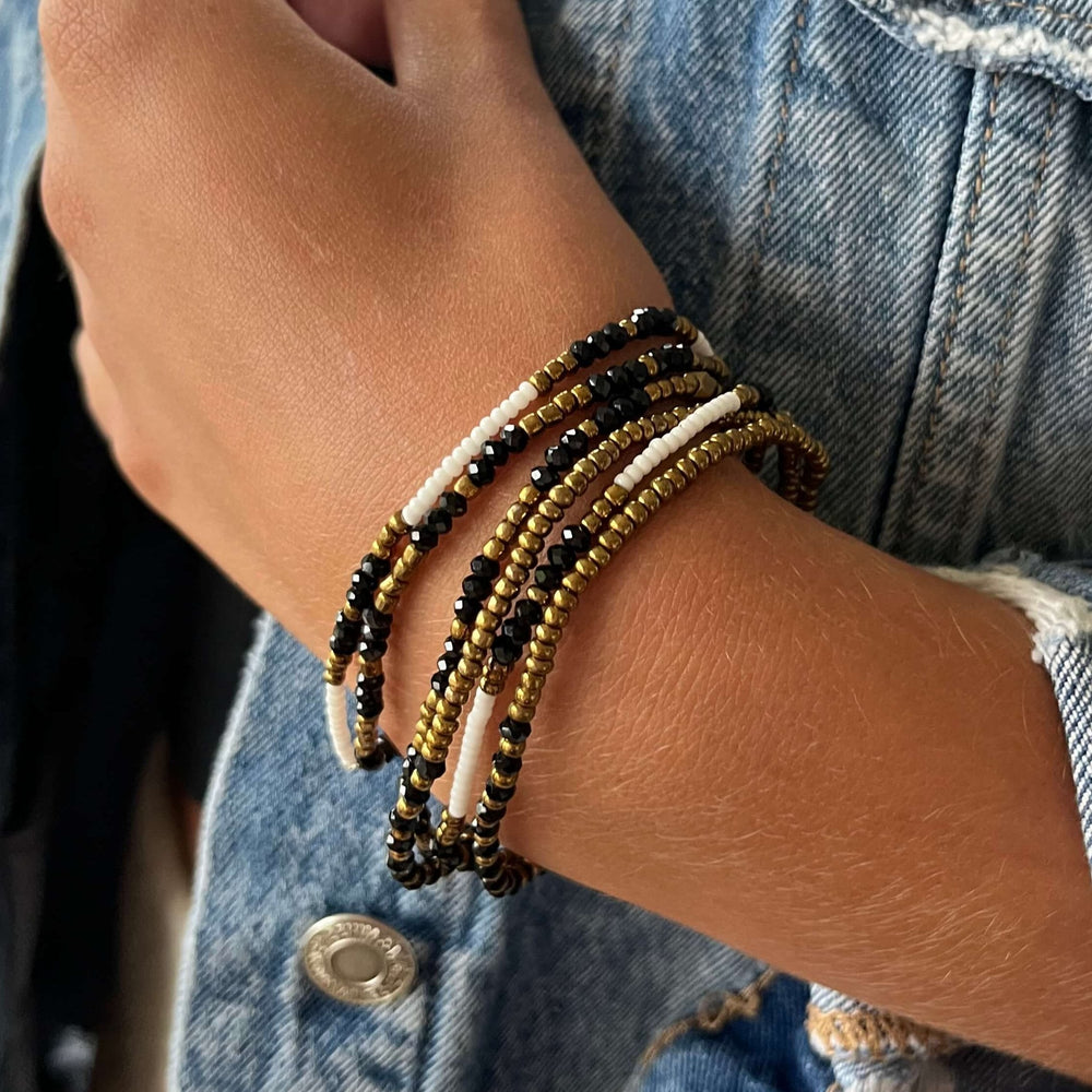 Close-up of a multi-strand stretchy beaded bracelet featuring gold, black, and white beads, designed as the Dusk Stretch Bracelet | Purpose Jewelry for stylish wellness accessories.