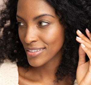 Close-up of a woman with glowing skin and curly hair, illustrating the effects of Golden Moon Dip® Illumination Mousse with Retinol + Wrinkle-Targeting Peptides | Farmhouse Fresh skincare product.