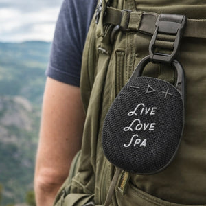 Wireless Clip Speaker | Live Love Spa attached to a backpack strap outdoors, portable wellness device for on-the-go audio during hikes or outdoor activities.