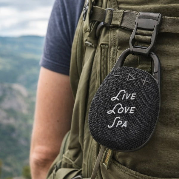 Wireless Clip Speaker | Live Love Spa attached to a backpack strap outdoors, portable wellness device for on-the-go audio during hikes or outdoor activities.