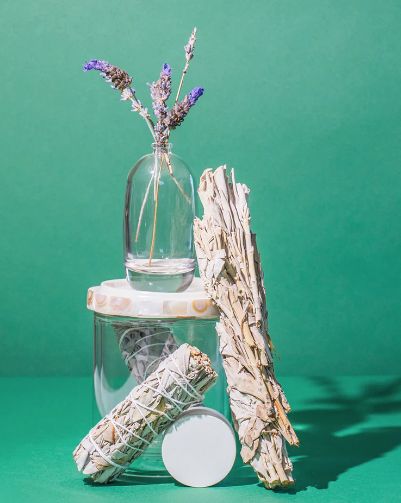 Clear glass jar with dried lavender flowers next to bundles of Palo Santo and sage, evoking natural wellness and relaxation, featuring Palo Santo Sage Rollerball Perfume Oil - Spirit | Hydra Bloom.