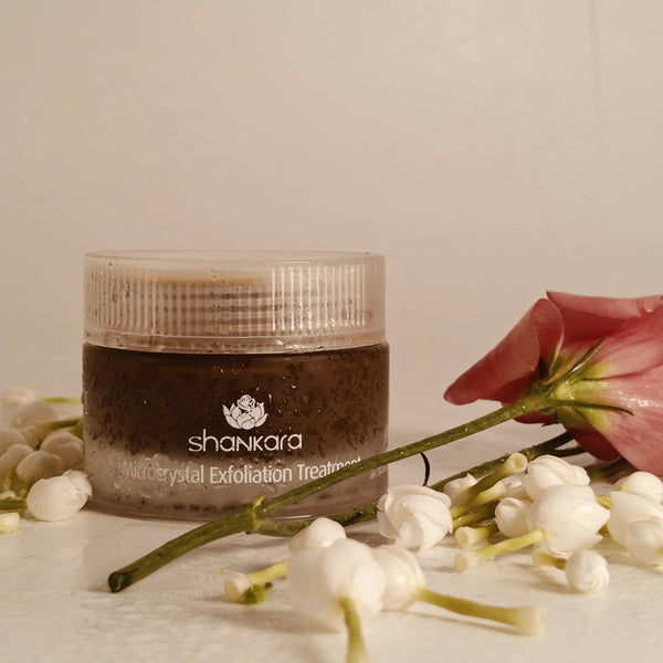 Microcrystal Exfoliator | Shankara jar surrounded by delicate white flower buds and a single pink flower, highlighting natural skincare and body care wellness.