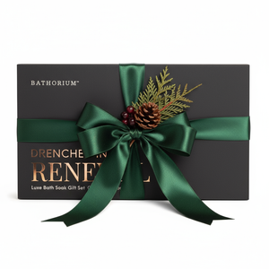 Black gift box wrapped with a dark green satin ribbon and decorated with pinecone and evergreen sprigs, featuring the Drenched In Renewal Gift Box Set | Bathorium logo.