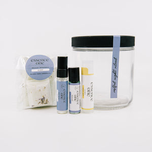 Ritual Kit | Essence One featuring a clear jar with black lid and pastel-labeled wellness supplements including sleep soak, roller, and balm for skincare and relaxation.