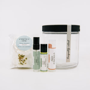 Ritual Kit | Essence One featuring a clear storage jar and a set of wellness items including shower steamers, aromatherapy sprays, and a lip balm.
