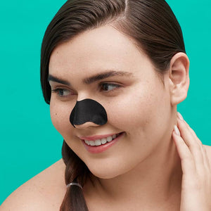 Woman with clear skin wearing a black charcoal nose strip, smiling gently, demonstrating skincare use with the Breakout Box 3-In-1 Acne Treatment Kit | Patchology.