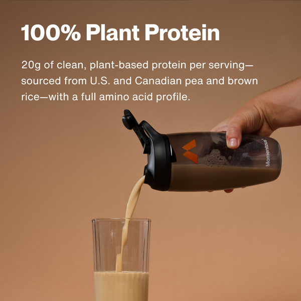 Hand pouring a creamy plant-based protein shake from a black shaker bottle labeled The Momentous Three - Vegan into a clear glass on a beige background with text highlighting 20g of clean plant protein per serving.