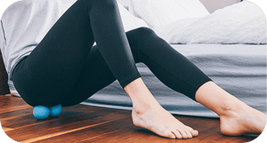 Person using a RAD Roller Soft | RAD for muscle recovery and body care on hardwood floor beside a bed, demonstrating wellness and relaxation at home.