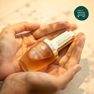 Hands gently holding a glass bottle of Timeless Kumkumadi Oil | Shankara with warm, natural lighting highlighting the skincare product and a Vogue Beauty Awards 2021 badge.