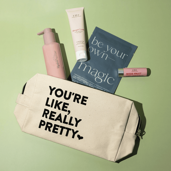 Canvas cosmetic bag with "You're Like, Really Pretty Bag | Live Love Spa" text printed, surrounded by skincare and wellness products on a light green background.