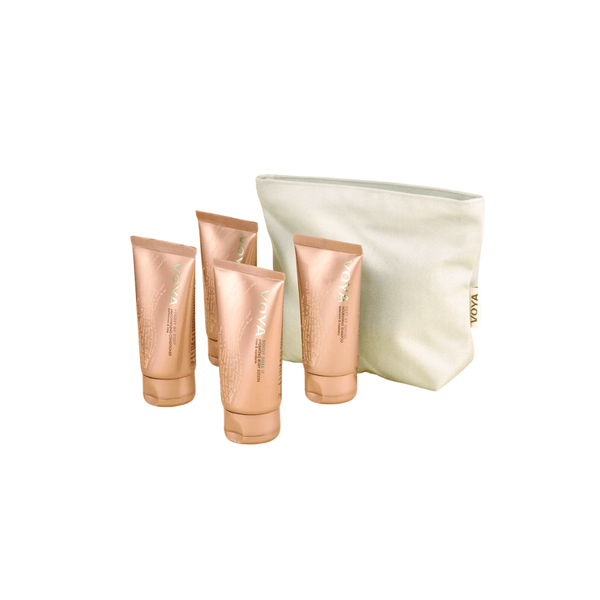 Four rose gold tubes of skincare products standing next to a cream-colored fabric pouch, representing the Organic Voyager Travel Set | VOYA for body care and wellness.