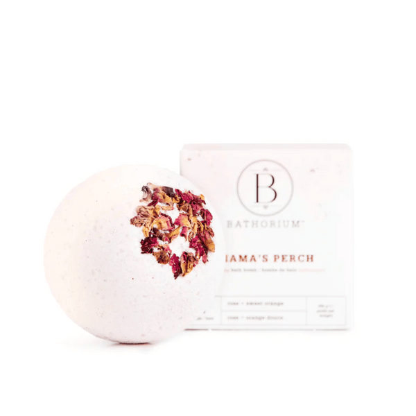 White bath bomb with dried rose petals on top next to its packaging labeled "Mama's Perch Bath Bomb | Bathorium," designed for skincare and wellness.