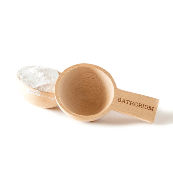 Wooden Crush Scoop | Bathorium, a natural wood scoop with the brand name engraved on the handle, shown empty and filled with white bath soak powder for skincare and body care use.