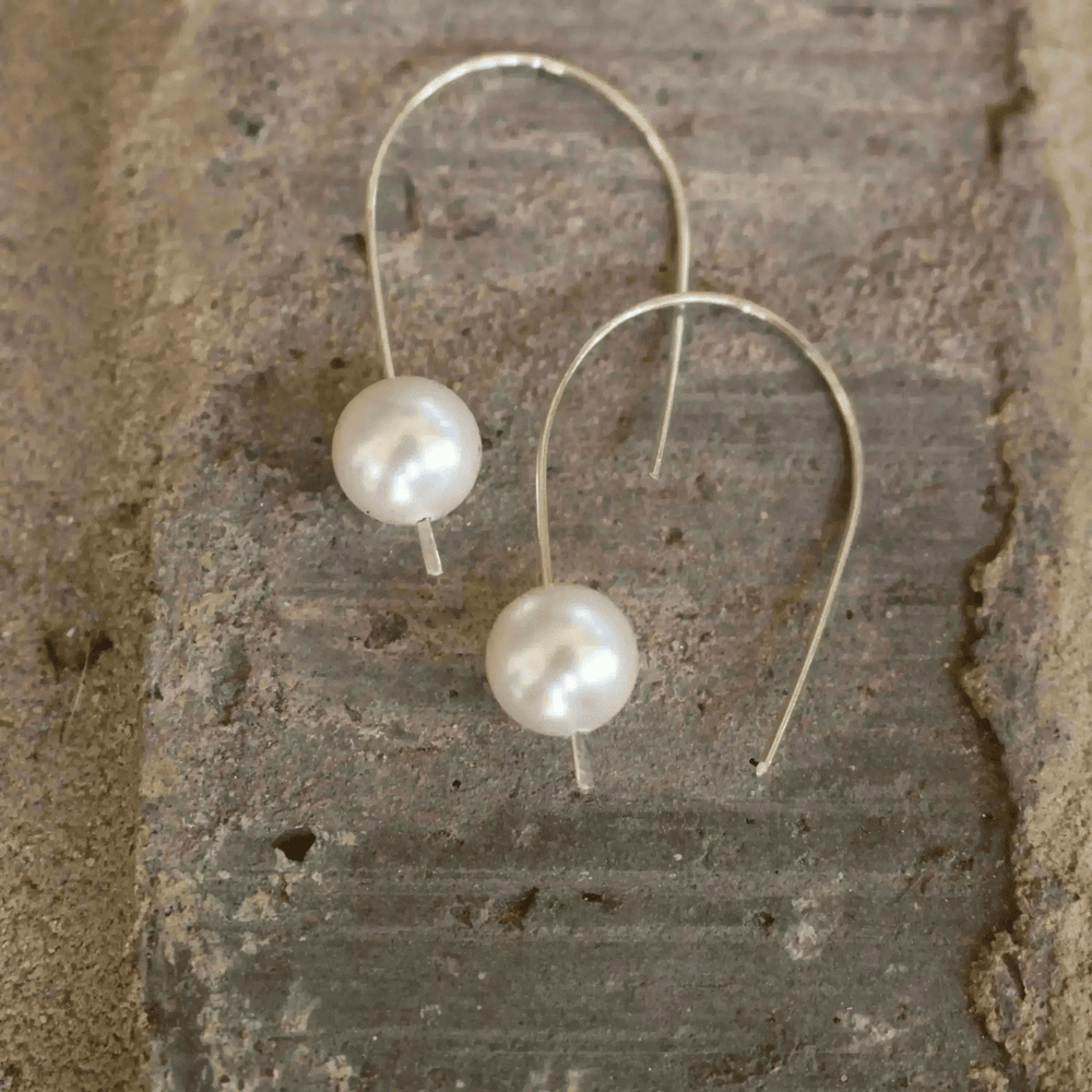 Madeline Pearl Drop Earrings | Liv & B featuring elegant white pearls on delicate silver hooks displayed on a rustic textured surface.