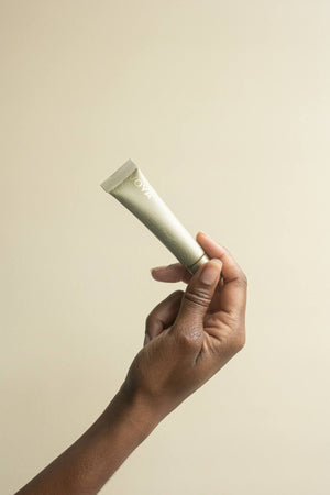 Hand holding a tube of Bright Eyes Regenerating Eye Cream | VOYA against a plain beige background, showcasing skincare product in a minimalistic style.