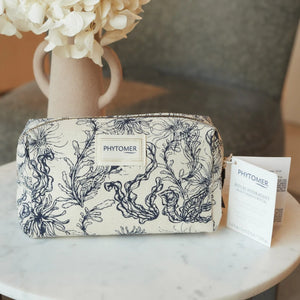 Seaside Moisturizing Starter Kit | Phytomer in a cream-colored pouch with dark blue seaweed pattern, displayed on a marble table with a beige vase of white flowers.