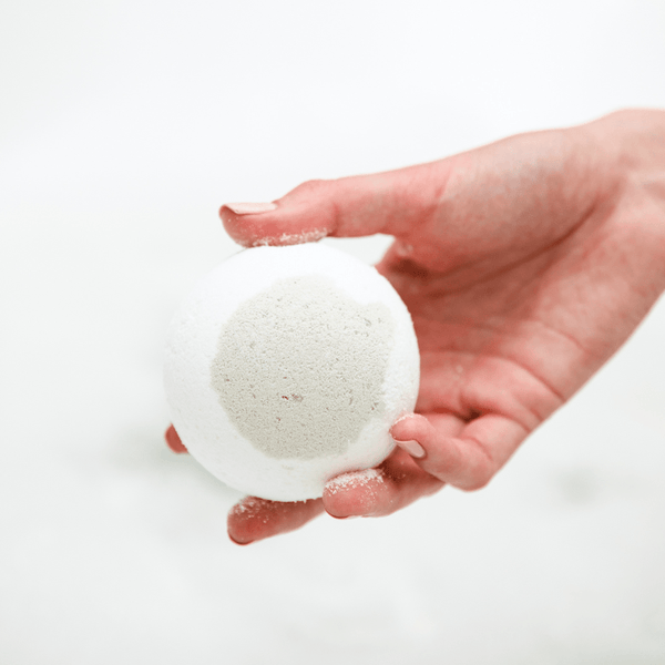 Hand holding a round white bath bomb with a light gray circular center, showcasing Boreal Fog Bath Bomb | Bathorium for skincare and wellness bath care.