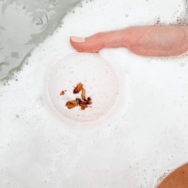 A hand gently holding a fizzing bath bomb with dried flower petals dissolving in bubbly water, showcasing Mama's Perch Bath Bomb | Bathorium for skincare and wellness.