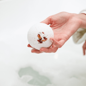 Hand holding a white spherical bath bomb with dried flower petals, ready to be used in a bath for a relaxing skincare experience with Mama's Perch Bath Bomb | Bathorium.