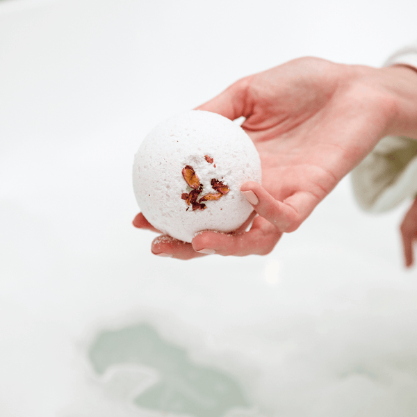 Hand holding a white spherical bath bomb with dried flower petals, ready to be used in a bath for a relaxing skincare experience with Mama's Perch Bath Bomb | Bathorium.