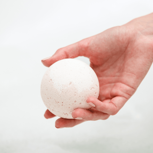 Hand holding a white spherical Pomelo Grove Bath Bomb | Bathorium against a soft, blurred background, emphasizing skincare and wellness body care.