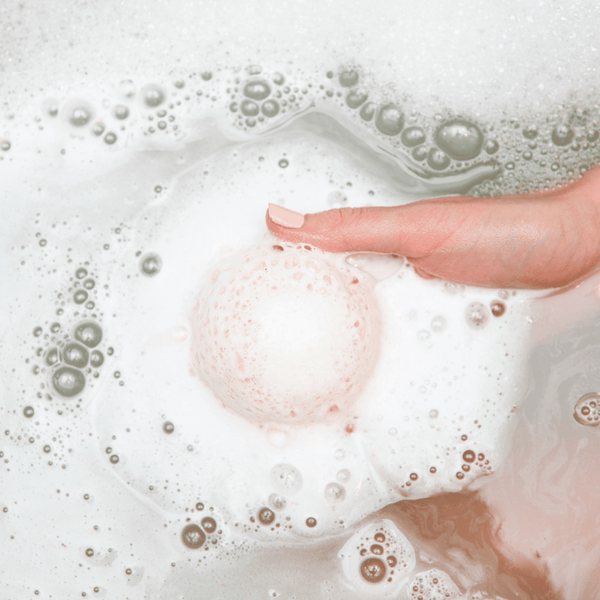 A hand gently holds a fizzing Pomelo Grove Bath Bomb | Bathorium releasing bubbles and foam in water, showcasing skincare and body care wellness.