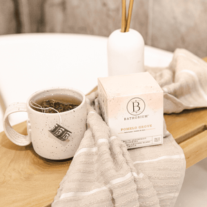 Pomelo Grove Bath Bomb | Bathorium box displayed on a wooden bath tray next to a cup of tea and a soft beige striped towel, creating a relaxing wellness atmosphere.