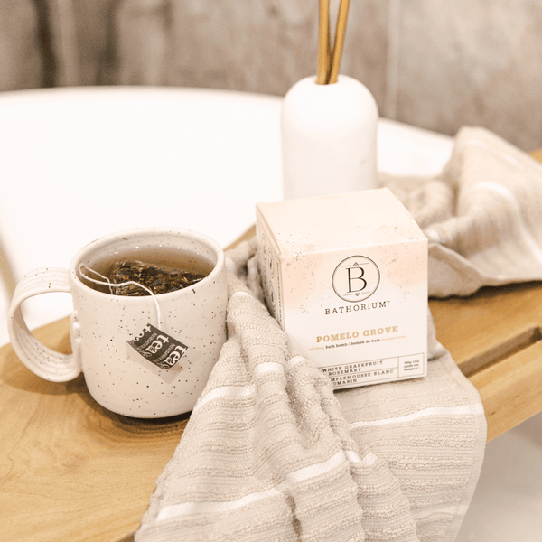 Pomelo Grove Bath Bomb | Bathorium box displayed on a wooden bath tray next to a cup of tea and a soft beige striped towel, creating a relaxing wellness atmosphere.