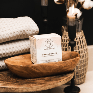 Pomelo Grove Bath Bomb | Bathorium displayed in a wooden bowl with stacked textured towels and a lit candle, evoking a serene spa-like atmosphere for skincare and body care wellness.
