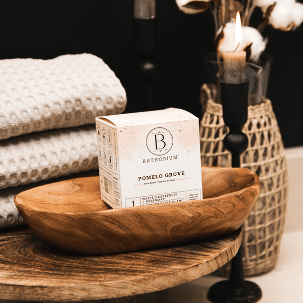 Pomelo Grove Bath Bomb | Bathorium displayed in a wooden bowl with stacked textured towels and a lit candle, evoking a serene spa-like atmosphere for skincare and body care wellness.