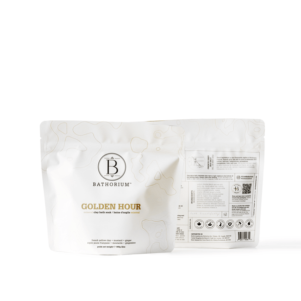 Two white resealable pouches of Golden Hour Clay Mineral Soak | Bathorium with subtle gold accents and product information on the back, promoting skincare and body care wellness.