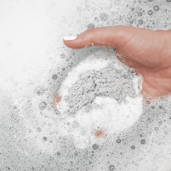 Hand holding a foaming granulated bath soak dissolving in water, showcasing Charcoal Garden Detox Crush | Bathorium for skincare and wellness.