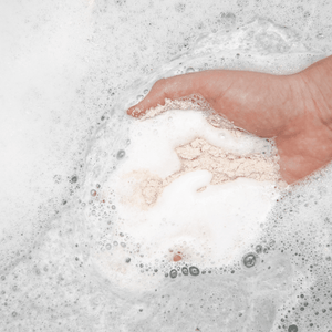 A hand holding a soft, powdery bath soak dissolving in water with gentle foam, showcasing a relaxing bath experience with Eucalyptus Apothecary Crush | Bathorium.