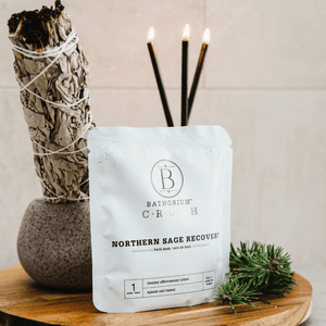 Northern Sage Recovery Crush | Bathorium bath soak package displayed on a wooden surface next to sage bundle, lit incense sticks, and green pine sprigs for a calming wellness skincare setting.