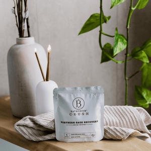 Northern Sage Recovery Crush | Bathorium bath soak packet displayed on a wooden surface with textured cloth, surrounded by greenery and soft natural light for a calming wellness setting